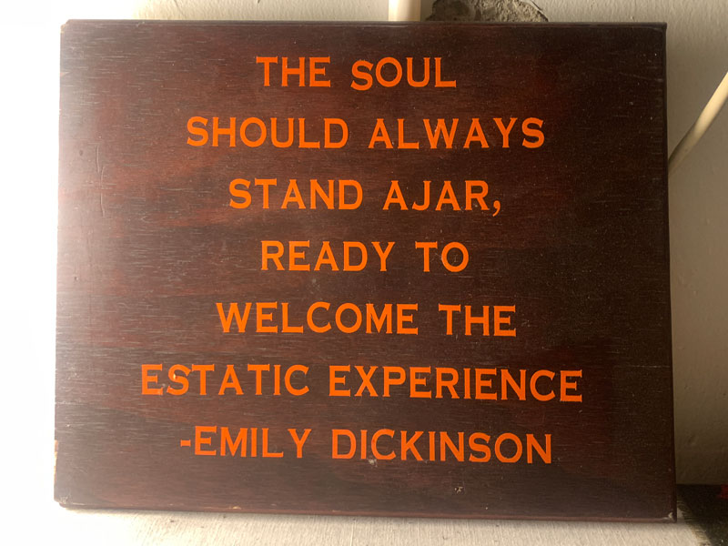 A brown sign with orange text reading: 'The soul should always stand a jar, ready to welcome to estatic experience. - Emily Dickinson'