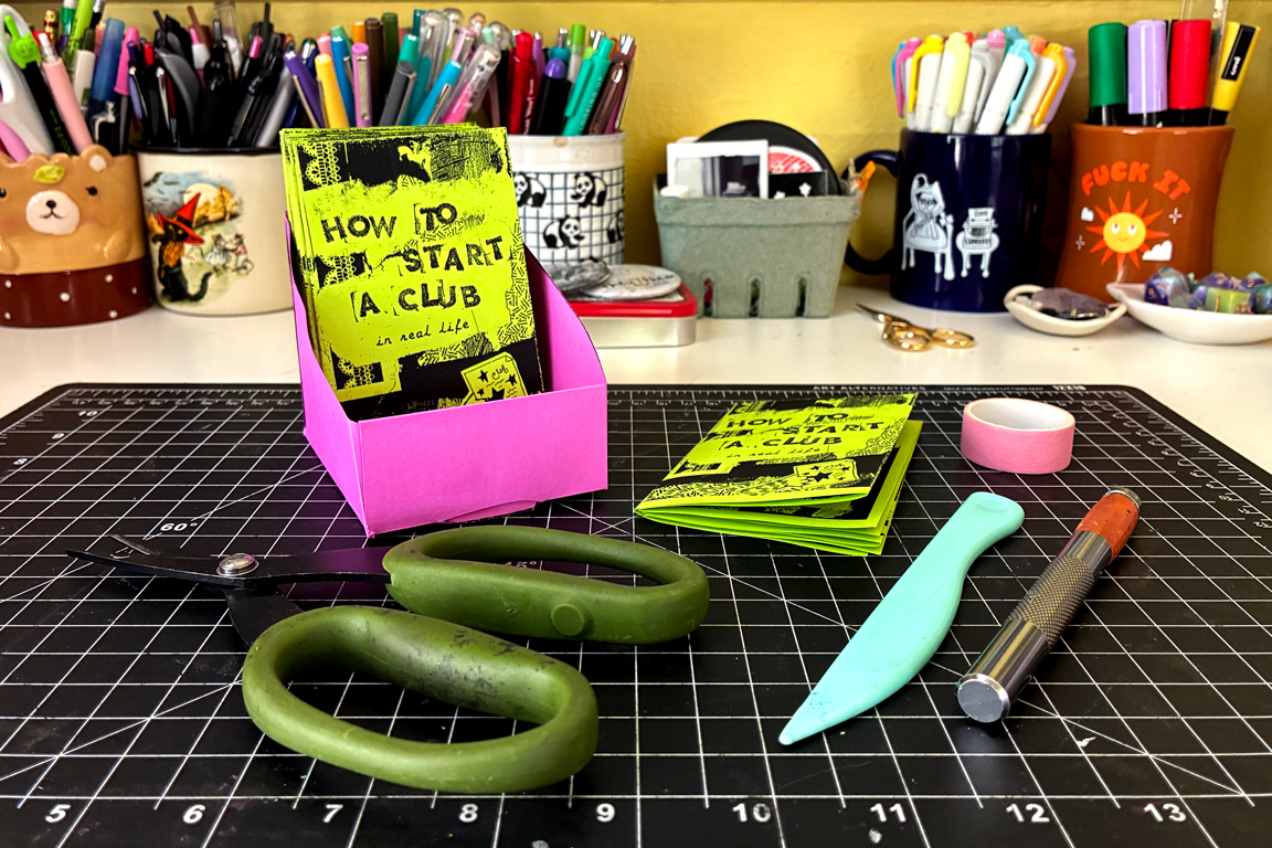 A pink paper zine holder and the supplies used to make it.