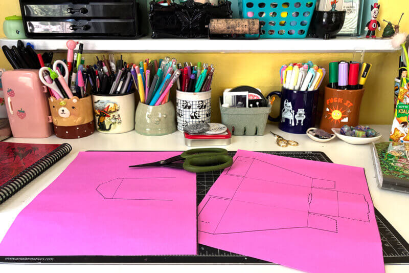 The template for a zine holder printed out on pink paper.
