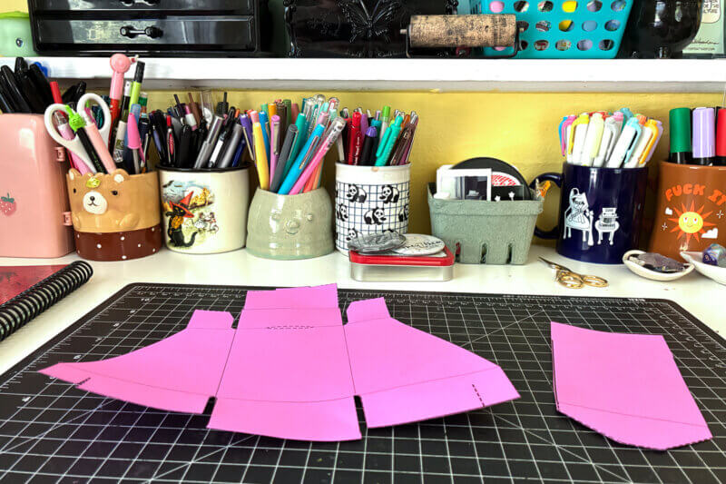 An unfolded zine holder cut out from pink paper.